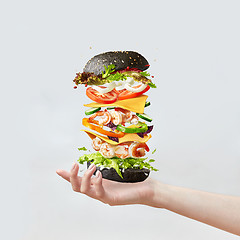 Image showing Woman\'s hand holds healthy sandwich from fresh seafood and vegetables on a light background.