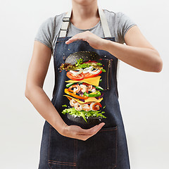 Image showing Woman holds a flying homemade burger from fresh organic ingredients on a light background.
