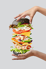 Image showing Flying burger with fresh ingredients between woman\'s hands on a light background.