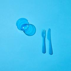 Image showing Plastic glass, fork and knife with shadows on a blue table.