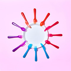 Image showing Multicolored plastic utensil around white plate on pink.