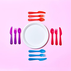 Image showing Multicolored plastic utensil around white plate on a light pink.