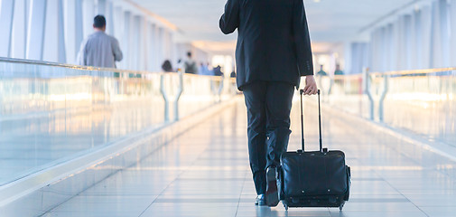 Image showing Businessman walking and wheeling a trolley suitcase at the lobby, talking on a mobile phone. Business travel concept.