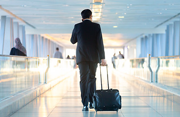 Image showing Businessman walking and wheeling a trolley suitcase at the lobby, talking on a mobile phone. Business travel concept.