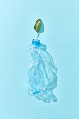 Image showing Used enpty plastic bottle with green leaf and shadows on blue.