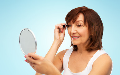 Image showing smiling senior woman with mirror applying mascara