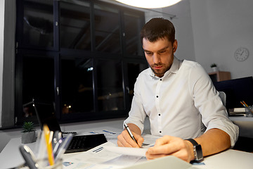 Image showing businessman with papers and laptop at night office