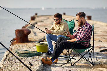 Image showing friends with smartphones fishing on pier at sea