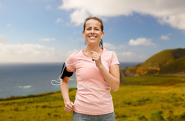Image showing woman with earphones and armband running outdoors