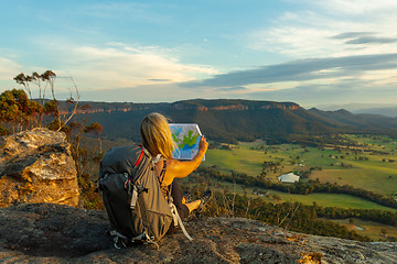 Image showing Hiker or tourist sitting on a rock using a map