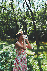 Image showing Active girl taking photo on instant camera in sunny forest