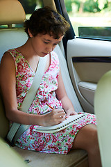 Image showing Thoughtful girl drawing in sketchbook in back seat of car