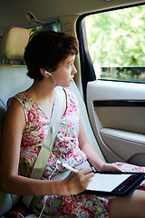 Image showing Creative girl in earphones looking at car window and drawing on tablet during road trip