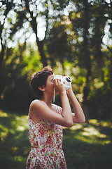 Image showing Active girl taking photo on instant camera in sunny forest