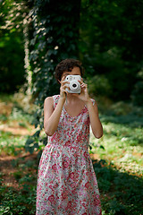 Image showing Smiling girl taking photo on instant camera in forest