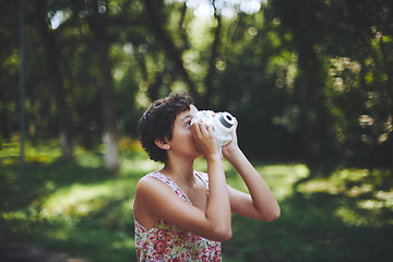 Image showing Active girl taking photo on instant camera in sunny forest