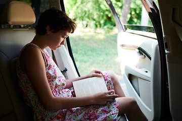 Image showing Enthusiastic girl reading book in car in trip