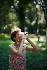 Image showing Active girl taking photo on instant camera in sunny forest