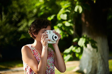 Image showing Active girl taking photo on instant camera in sunny forest