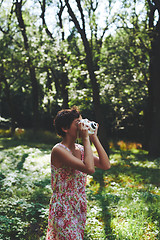 Image showing Active girl taking photo on instant camera in sunny forest