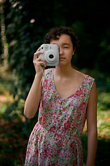 Image showing Smiling girl taking photo on instant camera in forest