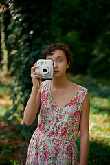 Image showing Smiling girl taking photo on instant camera in forest