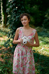 Image showing Smiling girl taking photo on instant camera in forest