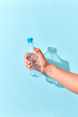 Image showing Hand crushes plastic bottle with shadow on a light blue.