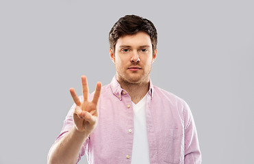 Image showing young man showing three fingers over grey