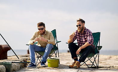 Image showing happy friends fishing and eating sandwiches