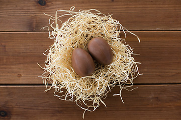 Image showing chocolate eggs in straw nest on wooden background