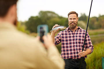 Image showing friend photographing fisherman with fish at lake