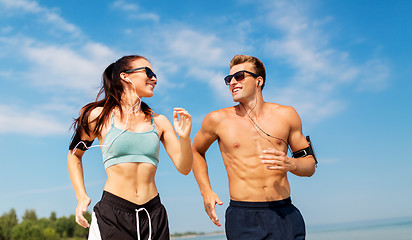 Image showing couple with phones and arm bands running on beach