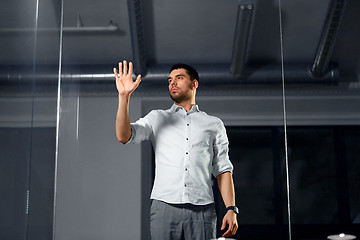 Image showing businessman touching glass wall at night office