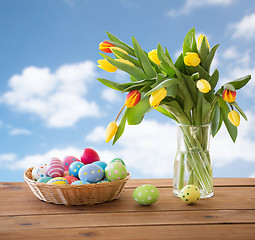 Image showing colored easter eggs in basket and flowers over sky