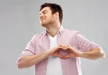 Image showing man making hand heart gesture over grey background