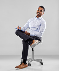 Image showing smiling indian businessman writing to clipboard