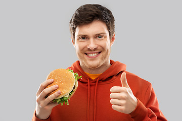 Image showing happy young man with hamburger showing thumbs up