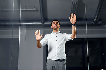 Image showing businessman touching glass wall at night office