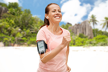 Image showing woman with earphones and armband running on beach