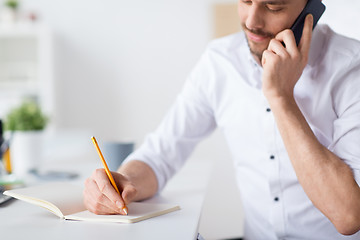 Image showing businessman calling on cell writing to notebook