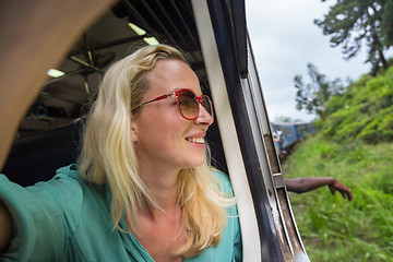 Image showing Happy smiling woman looks out from window traveling by train on most picturesque train road in Sri Lanka