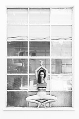 Image showing Fit sporty active girl in fashion sportswear doing yoga fitness exercise in front of big industrial window frame. colorful reflections in window glass. Urban style yoga. Black and white