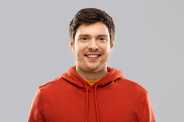 Image showing smiling young man in red hoodie over grey