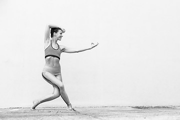 Image showing Fit sporty active girl in fashion sportswear doing yoga fitness exercise in front of gray wall, outdoor sports, urban style. Black and white photo.