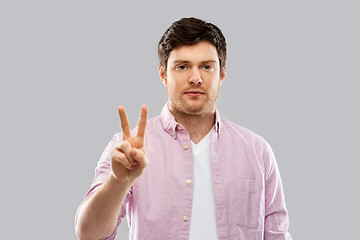 Image showing young man showing two fingers over grey background