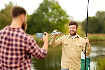 Image showing friend photographing fisherman with fish at lake