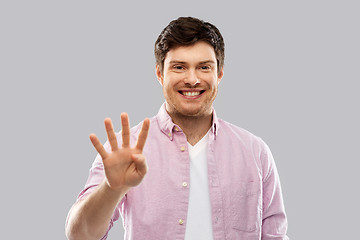 Image showing young man showing four fingers over grey