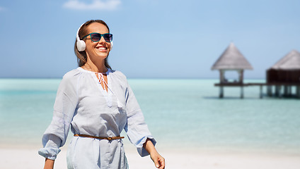 Image showing woman with headphones walking along summer beach