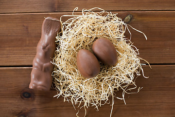 Image showing chocolate bunny and eggs in straw nest on wood